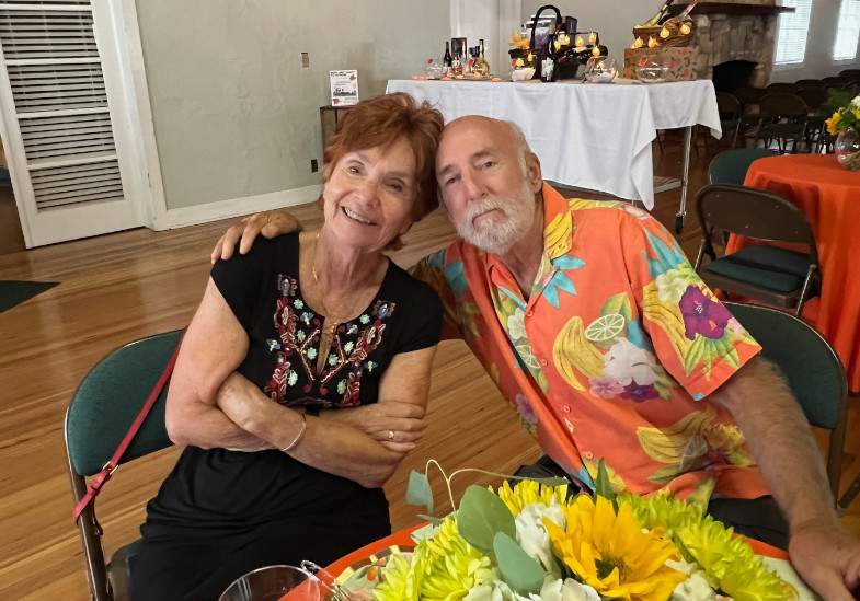 Steve & Fredda sitting at a table hugging and smiling